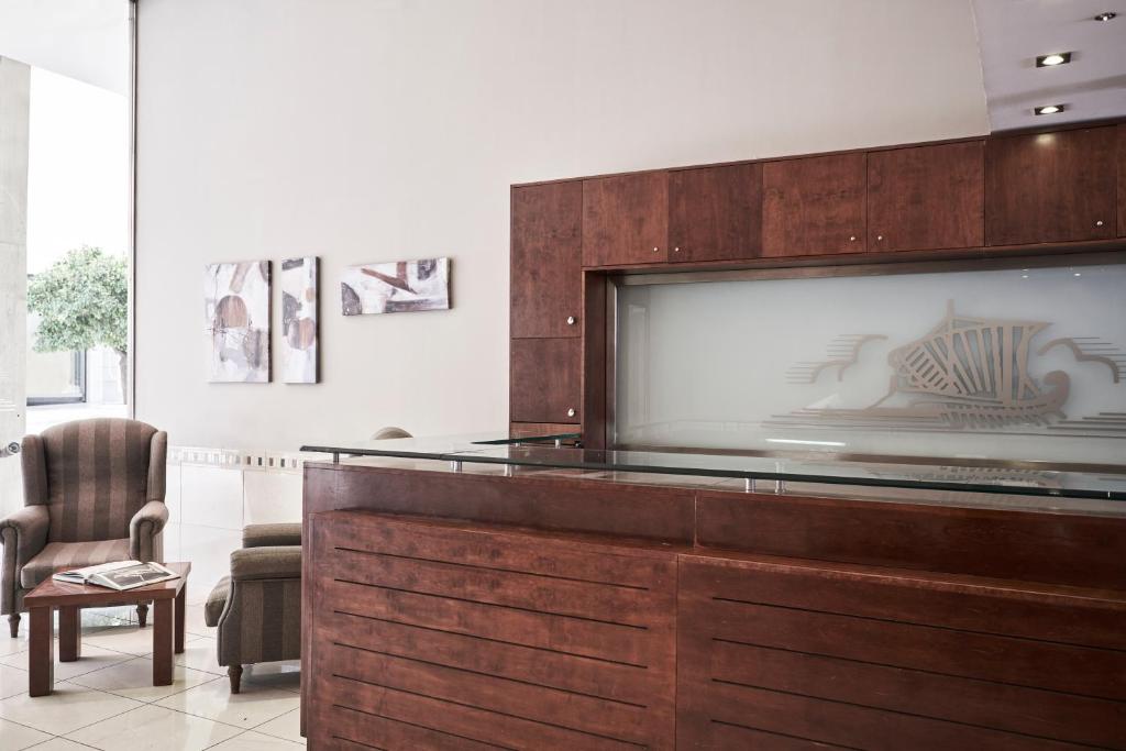 Mūsdienīga viesnīcas reģistratūra ar koka un stikla elementiem, kurā ir ērtas atpūtas zonas un mākslas darbi uz sienām.