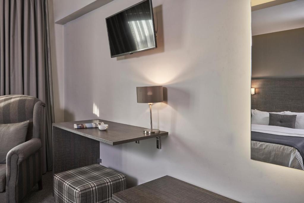 Mūsdienīga viesnīcas istaba ar ērtu krēslu, galdu un televizoru, kas nodrošina komfortablu un relaksējošu atmosfēru. Interjers ir elegantā krāsā ar plūstošām aizkaru drānām.