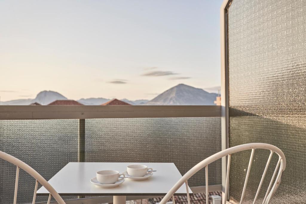Balcony setting with two coffee cups on a white table, offering a scenic view of mountains and a clear sky. Perfect for relaxation and enjoying a morning coffee.