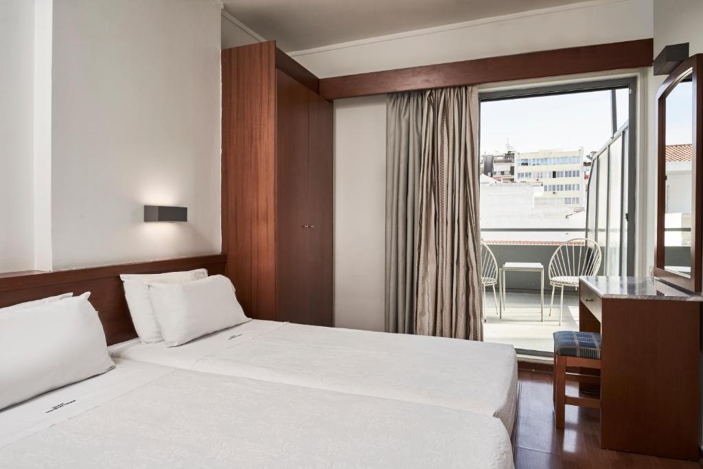 Mūsdienīgs viesnīcas numurs ar divām gultām, koka mēbelēm un lielu logu, kas ved uz balkonu. Numurā ir arī tualetes galdiņš un aizkari.