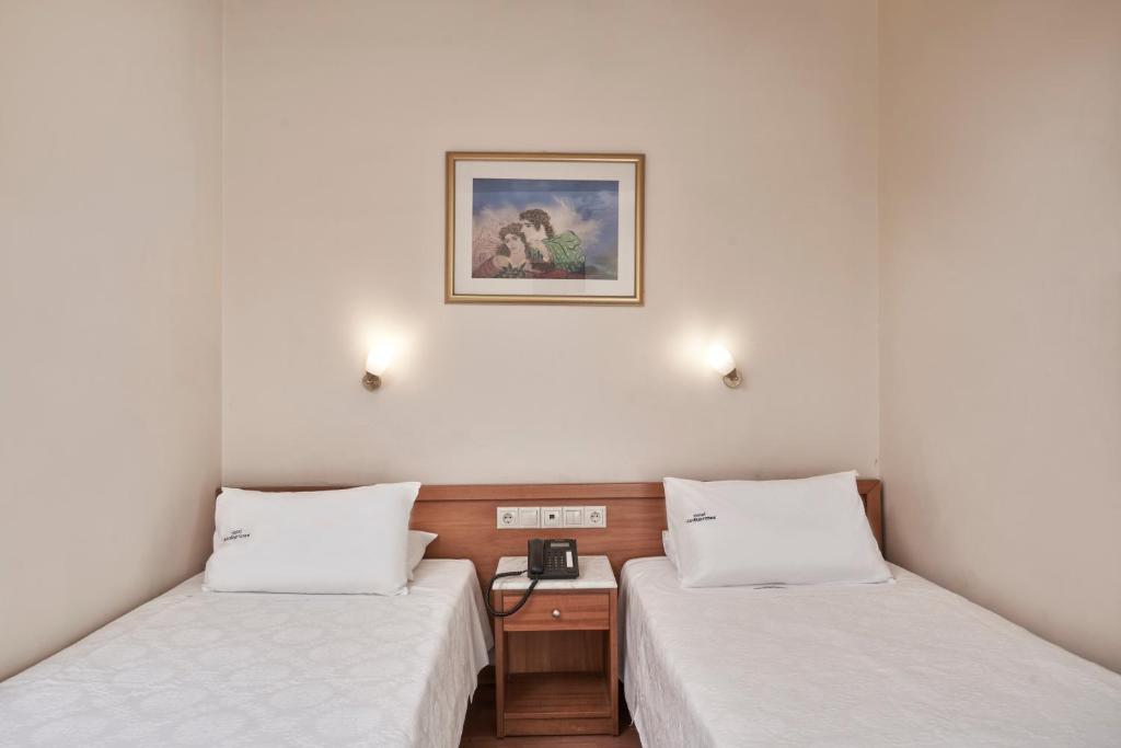 Divvietīga guļamistaba ar divām atsevišķām gultām, koka naktsgaldiņu un gaismas ķermeņiem pie sienām. Sienā ir mākslas darbs, kas piešķir telpai mājīgu atmosfēru.