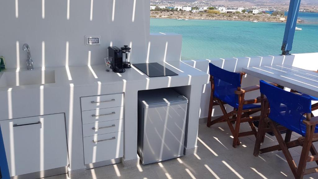 Mūsdienīga virtuve ar jūras skatu, kas iekārtota ar baltu galdu, krēslām un modernām ierīcēm. Gaismas un ēnas spēle rada patīkamu atmosfēru.