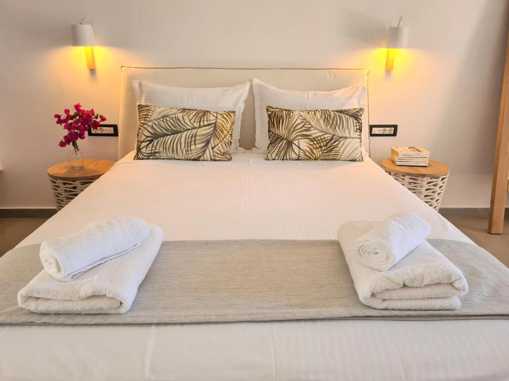 Mūsdienīga guļamistaba ar ērtu gultu, palmām rotātām spilveniem un tīrām dvieļiem uz gultas. Siltas gaismas un ziedi papildina mājīgu atmosfēru.