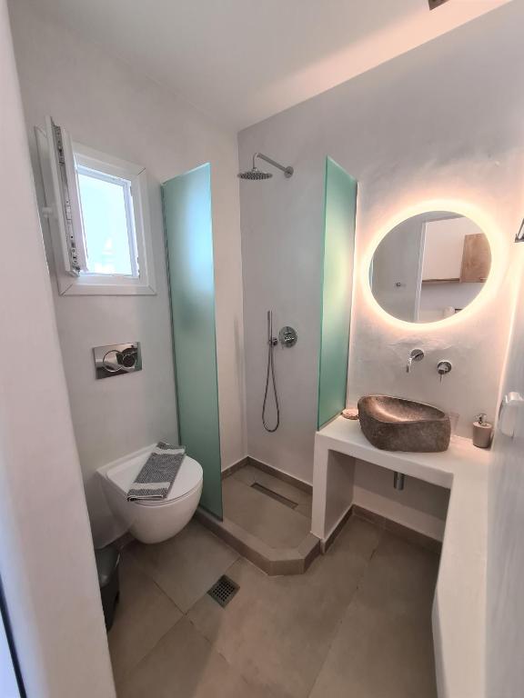 Moderns vannas istabas interjers ar dušu, pelēku akmens izlietni un apaļu gaismas spoguli. Gaiši toņi un stikla paneļi rada svaigu un atvērtu atmosfēru.