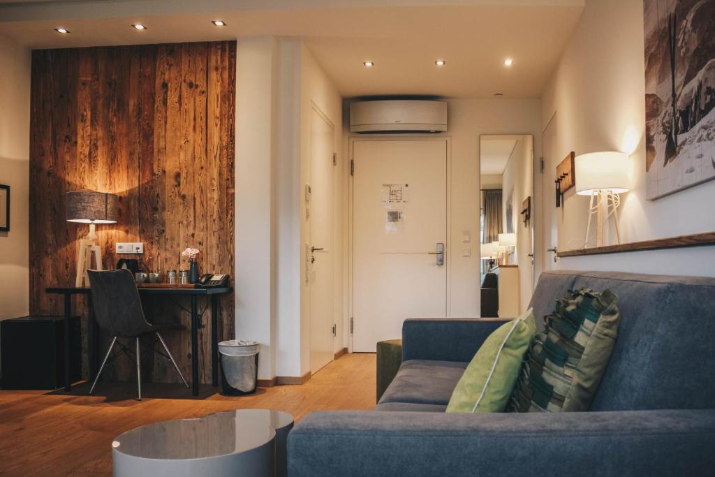 Mūsdienīga viesnīcas istaba ar koka sienu, rakstāmgalds un ērta dīvāna zona. Interjerā ir gaismas un mājīga atmosfēra.