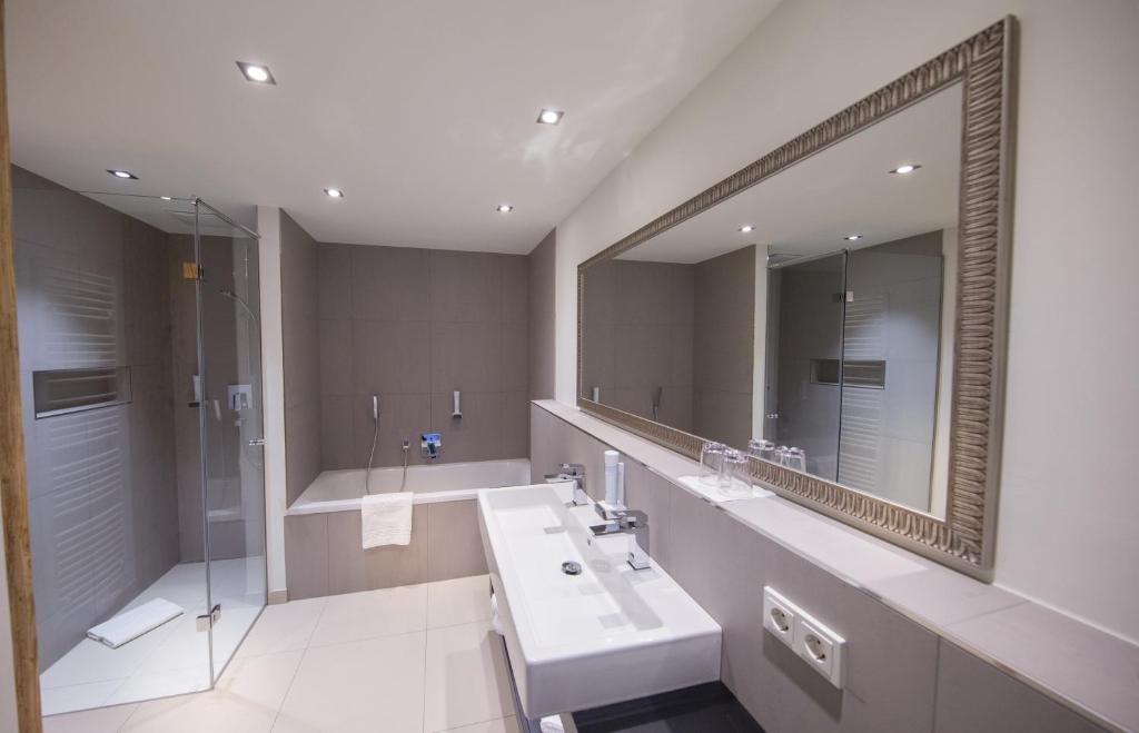 Mūsdienīgs vannas istabas interjers ar stikla dušu, vannu un plašu spoguli. Gaismas elementi un neitrāla krāsu palete rada elegantu atmosfēru.