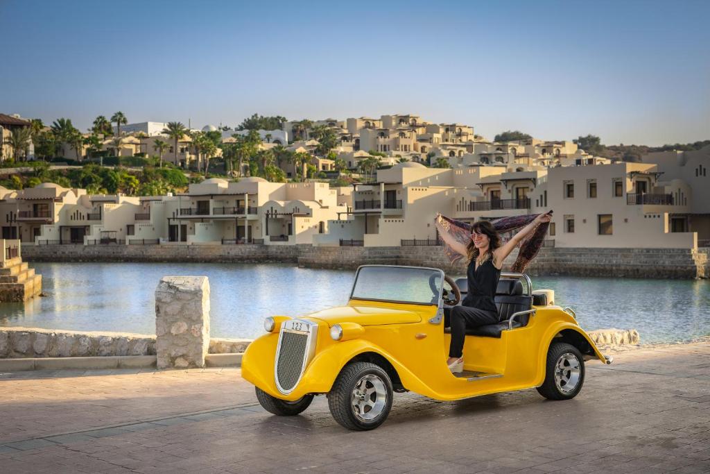 Sieviete dzeltenā retro auto pie Cove Rotana Resort piekrastē