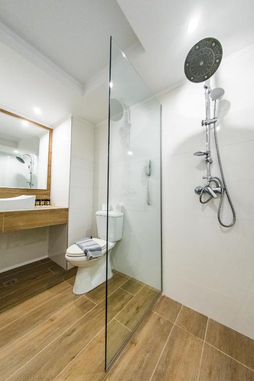 Mūsdienīgs vannas istabas interjers ar stikla dušas kabīni, tualeti un koka izskata grīdu. Svaiga un gaiša atmosfēra ar elegantu spoguli un modernu santehniku.