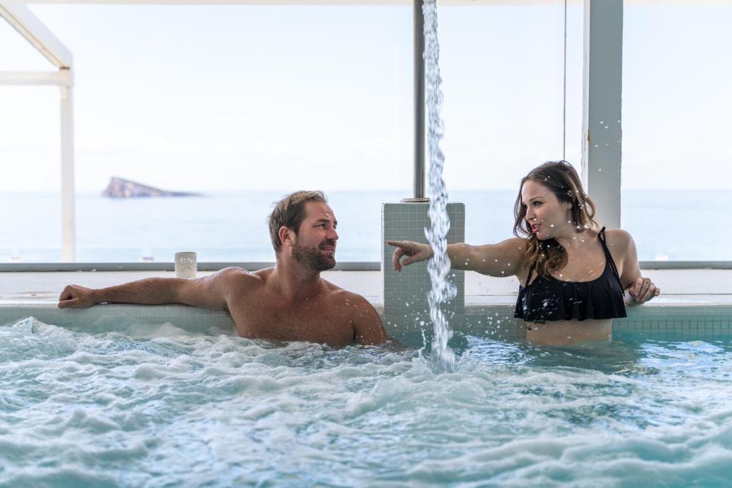 Pāris relaksējas džakuzi, izbaudot skatu uz jūru, un sarunājas, kamēr ūdens plūst no strūklakas.