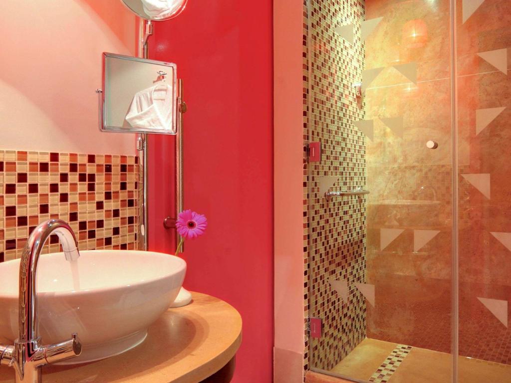 Moderns vannas istabas interjers ar sarkanu sienu, stilīgu washbasin un dušu ar mozaīkas flīzēm. Zieds pie washbasin piešķir dzīvīgumu.