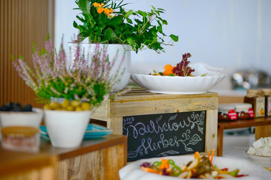 Svaigu dārzeņu un ziedu dekorācija uz koka galda, ar krāsainiem traukiem un uzrakstu "Delicious Herbs".