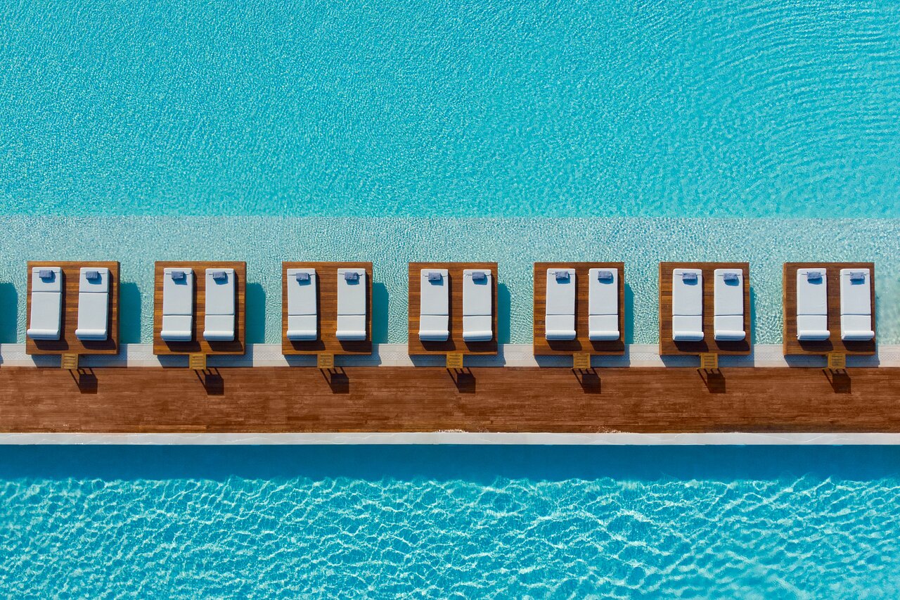 Baseina zona ar saulessargiem un spilveniem, kas izvietoti gar ūdens virsmu. Klarity ūdens un koka dēļu celiņš veido relaksējošu atmosfēru. panoramic view with beach and pools