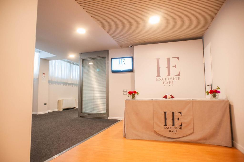 Mūsdienīga viesnīcas reģistratūra ar elegantu dizainu, kurā redzama informācijas tāfele un ziedi uz letes.