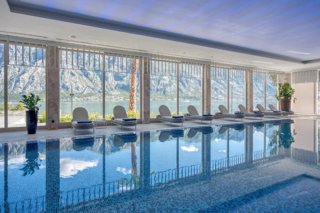 Luksusa spa telpa ar peldbaseinu un panorāmas skatu uz kalniem un ūdeni, nodrošinot relaksējošu atmosfēru. Gaismas un interjera dizains rada mierīgu noskaņu.