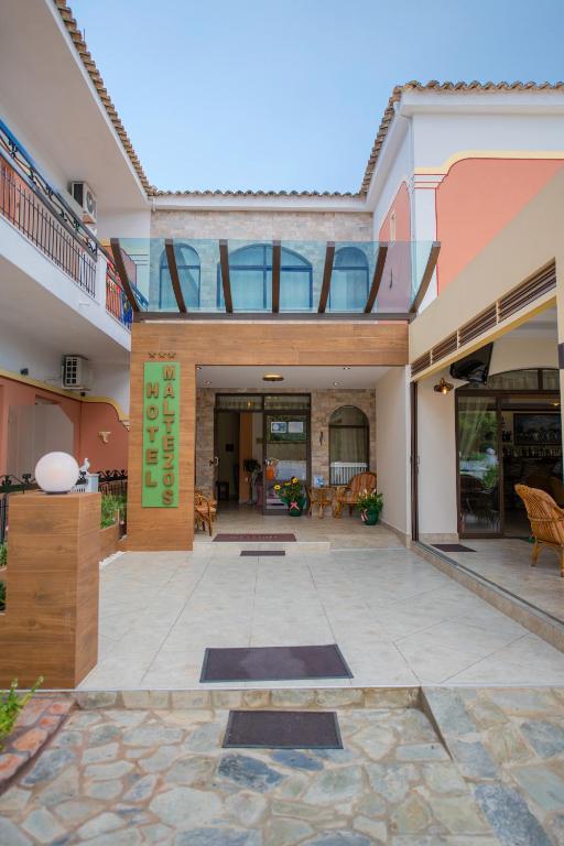 Mūsdienīgs viesnīcas ieejas dizains ar stikla elementiem un koka akcentiem, kas rada viesmīlīgu atmosfēru. Vides apstādījumi un sēdvietas pie ieejas papildina kopējo tēlu.