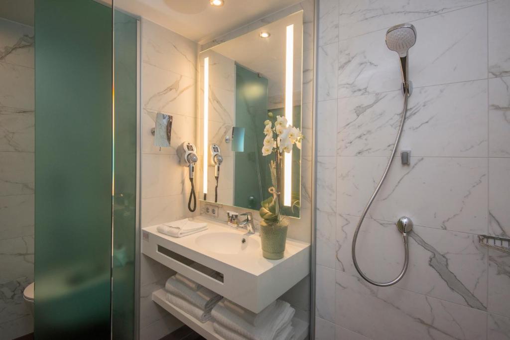 Mūsdienīgs vannas istabas interjers ar marmora sienām, dušu un minimālistisku izskatu. Uz galda izvietoti dvieļi un zieds, radot relaksējošu atmosfēru.