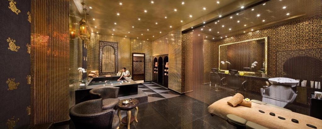 Elegants un grezns spa interjers ar zeltainām flīzēm un mīkstām mēbelēm, nodrošinot relaksāciju un komfortu. Gaismas un dekorācijas rada mierīgu atmosfēru.