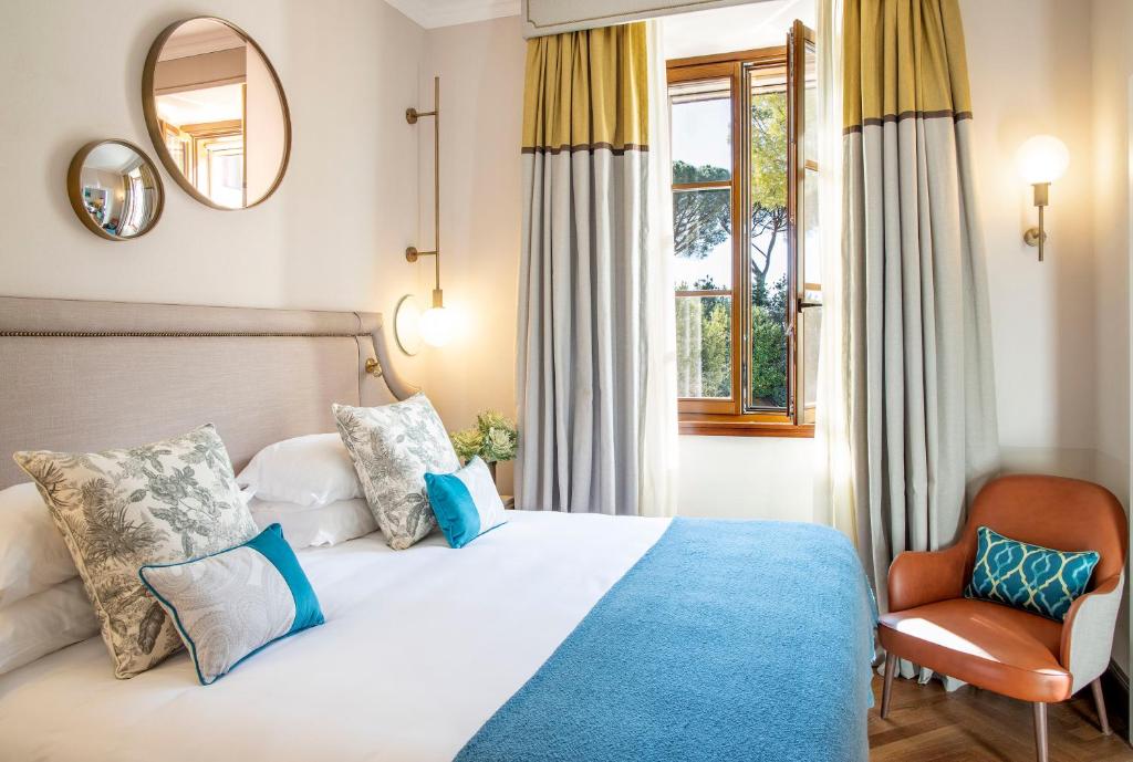 Mūsdienīgs guļamistabas interjers ar gultu, dekoratīvām spilveniem un logu, kas paver skatu uz dabu. Telpā ir siltas krāsas un eleganti apgaismojumi.