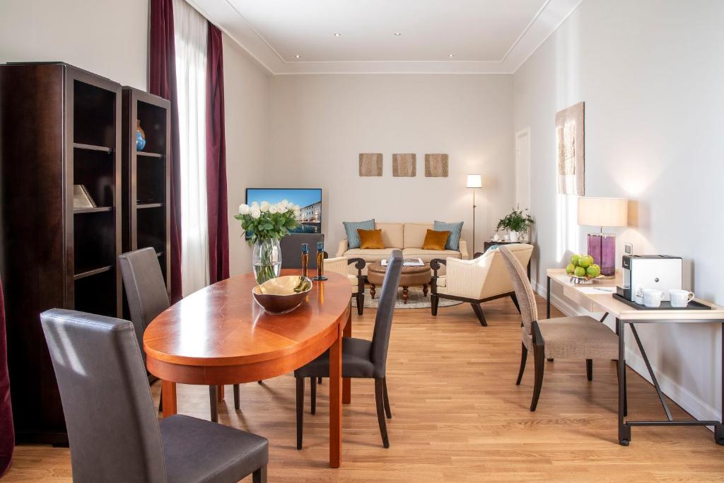 Mūsdienīgs dzīvojamās telpas interjers ar koka galdu, ērtām mēbelēm un dekoratīviem elementiem. Telpa ir gaiša un plaša, ar logiem, kas nodrošina dabisko apgaismojumu.