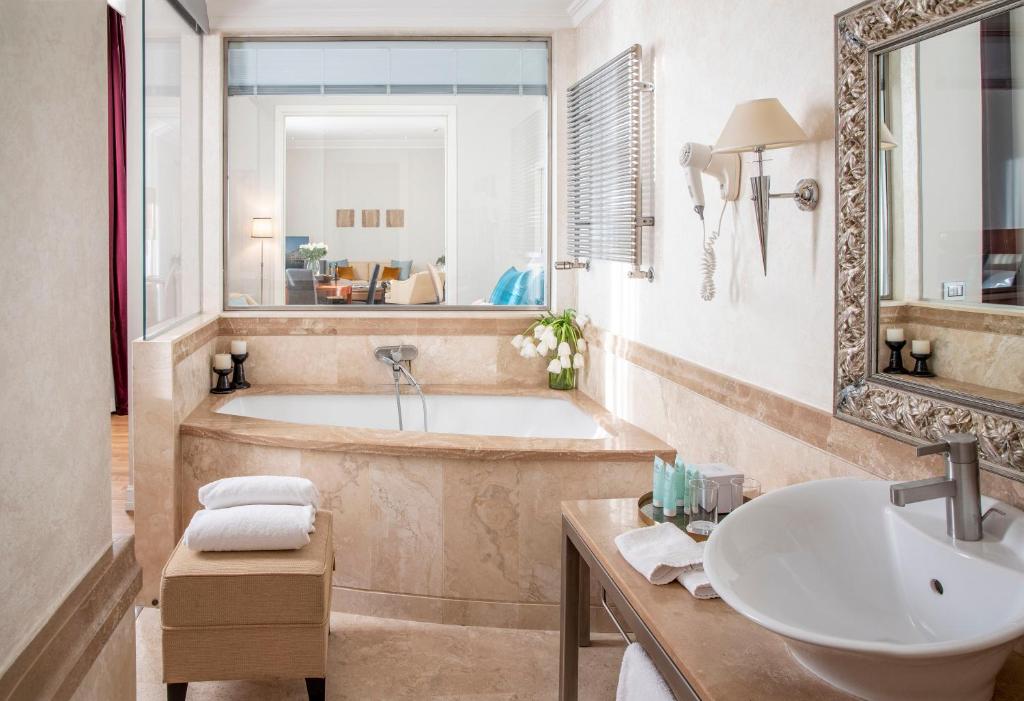 Mūsdienīga vannas istaba ar elegantu marmora apdari, vannu un mūsdienīgu izlietni. Telpā ir daudz gaismas un grezni aksesuāri, radot relaksējošu atmosfēru.