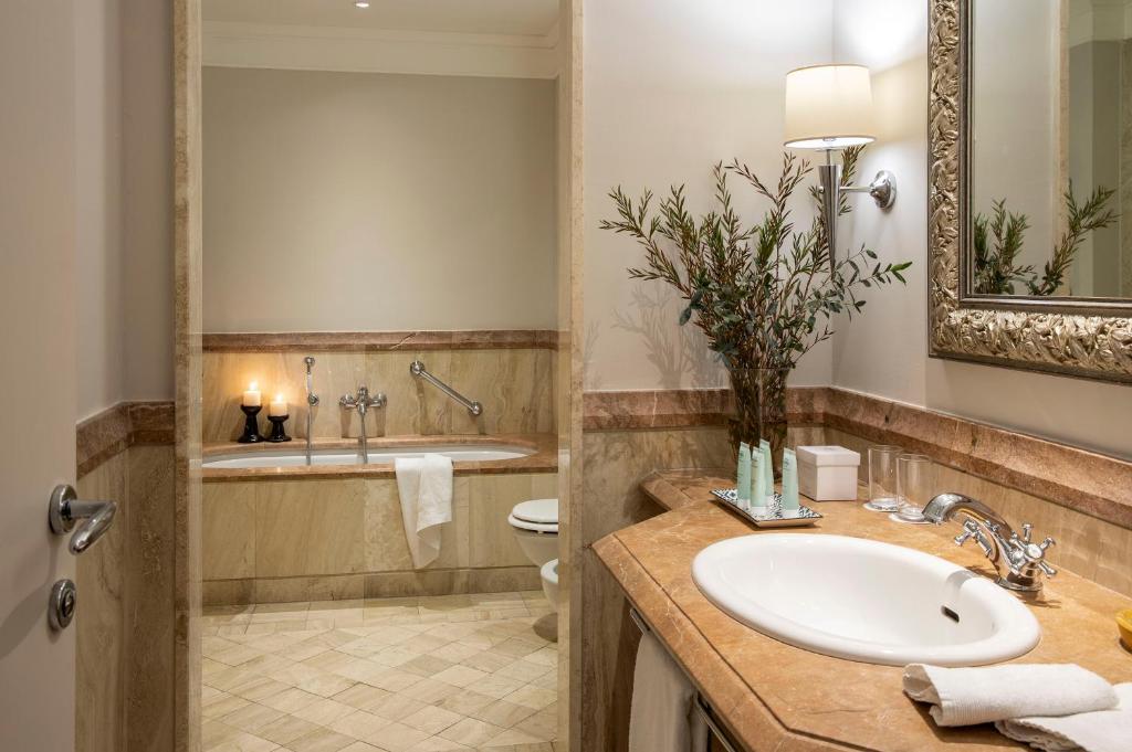 Elegants vannas istabas interjers ar marmora detaļām, vannu un dekoratīvām svečturiem. Vannas istabā redzams arī krāšņs spogulis un zaļi augi, kas piešķir svaigumu.