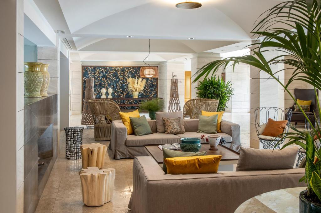 Mūsdienīgs viesnīcas interjers ar ērtām dīvānu grupām, dekoratīviem spilveniem, augiem un stilīgu mākslu uz sienas. Telpa ir gaiša un aicinoša, radot relaksējošu atmosfēru.