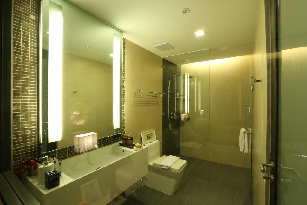 Mūsdienīgs vannas istabas interjers ar stikla dušu, elegantu izlietni un modernām apgaismojuma ierīcēm. Siltas krāsas un minimālistisks dizains rada relaksējošu atmosfēru.