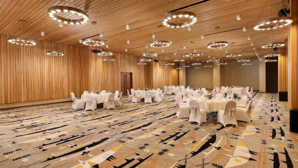 Eleganta pasākumu telpa ar apaļiem galdiem un stilīgām gaismām, radot modernu un viesmīlīgu atmosfēru. Ideāli piemērota svinībām un konferencēm.