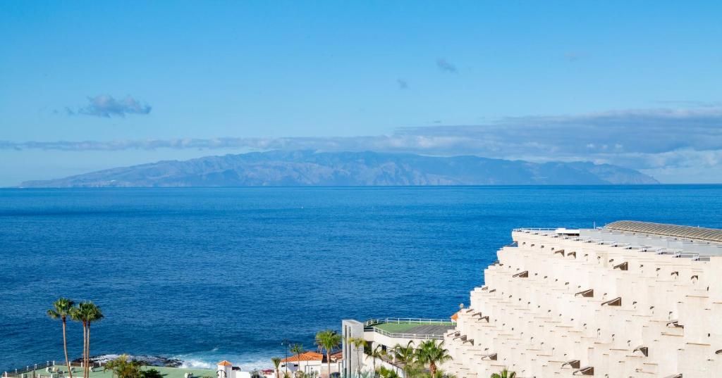 Skats uz mierīgu jūru ar kalnu salu fona. Priecīgas palmas un moderna arhitektūra pie krasta.