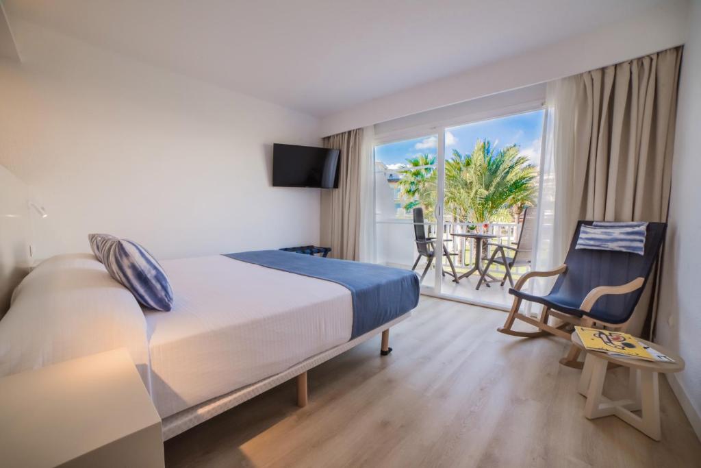 Mūsdienīgs viesnīcas numurs ar divguļamo gultu, televizoru un skatu uz terasi ar palmu kokiem. Telpā ir gaišs interjers un ērta atpūtas zona.