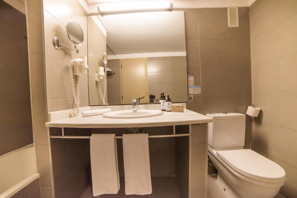 Mūsdienīgs vannas istabas interjers ar gaišām flīzēm, izsmalcinātu izlietni un higiēnas līdzekļu komplektu. Vannas istabā ir arī tualete un spogulis.