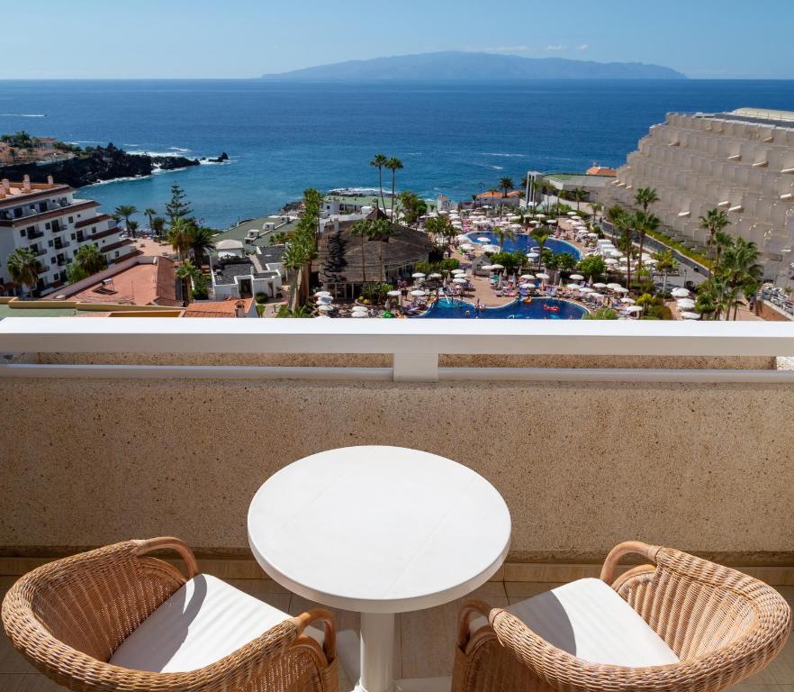 Skats no balkona uz jūru, baseinu un viesnīcu kompleksu, ar palmām un saulainu laiku. Ideāla vieta relaksācijai un brīvdienu plānošanai.