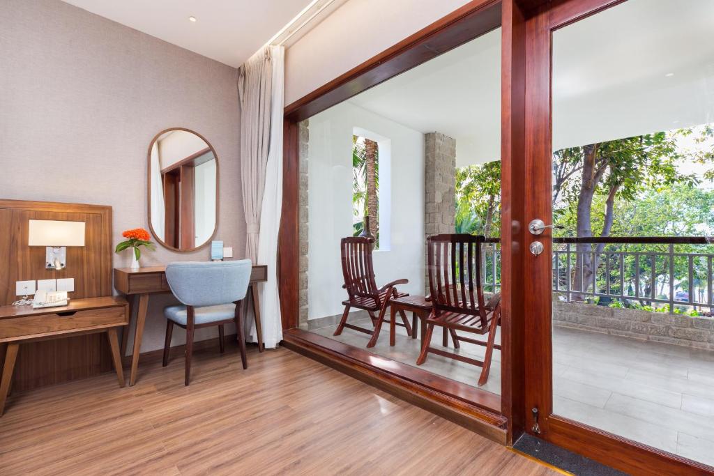 Mūsdienīgs viesnīcas numurs ar rakstainu koka grīdu, galdu un krēslu, kur blakus ir spogulis un balkons ar divām koka krēslām.