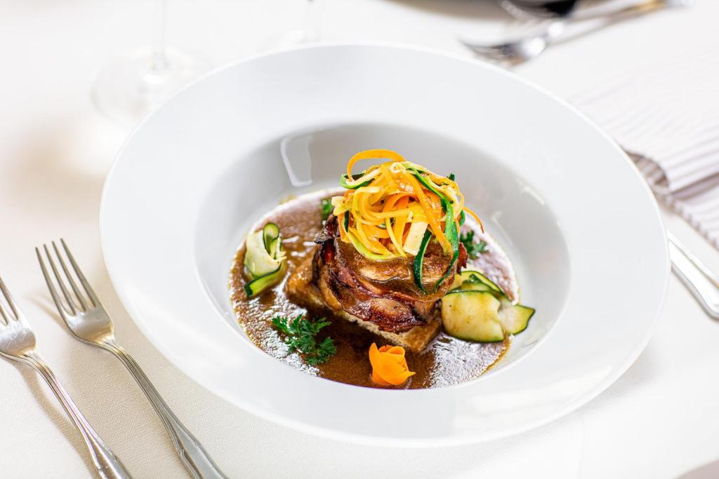 Elegants ēdiens ar gaļas porciju, dekorētu ar dārzeņu svītrām un mērci, pasniegts uz baltas porcelāna šķīvja.