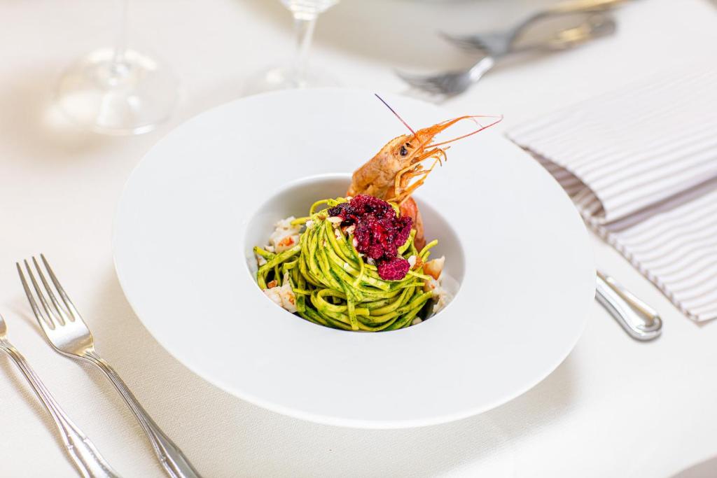 Zaļie makaroni ar garnelēm un aveņu mērci, pasniegti elegantā baltā šķīvī.