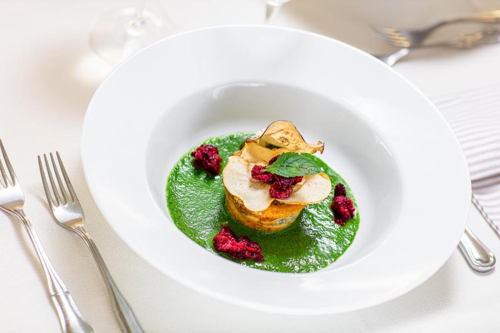 Gurķu mērce ar ceptu dārzeņu pudiņu, dekorēts ar žāvētām ogām un piparmētru lapām. Elegantais servējums uz baltas šķīvja piešķir izsmalcinātību.