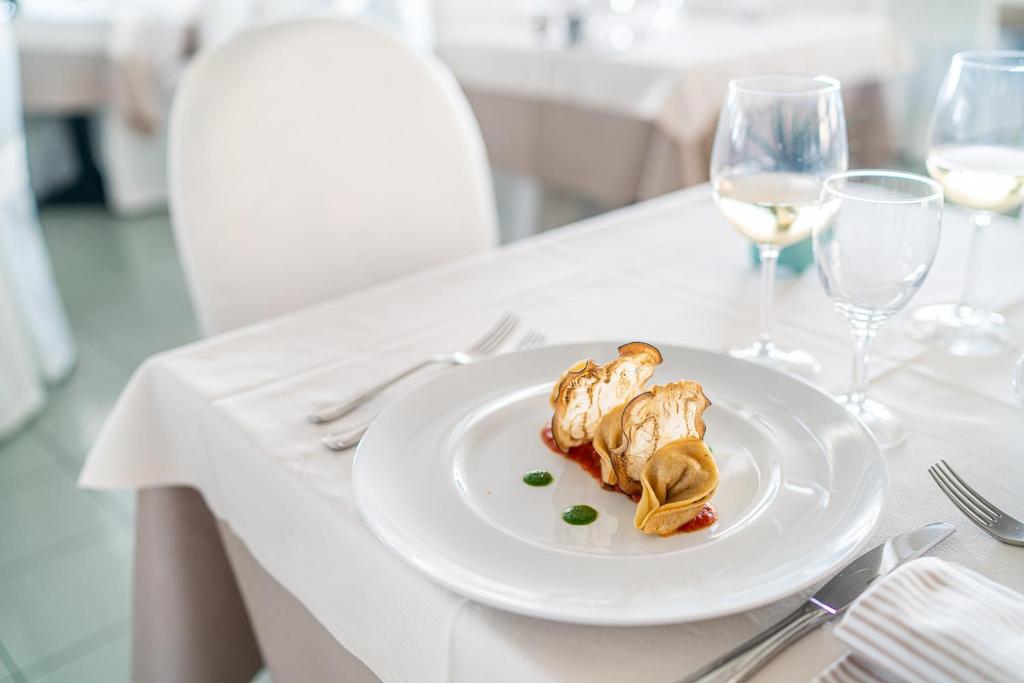 Grezns ēdiens uz baltā šķīvja, pasniegts eleganti noformētā restorānā. Šķīvī redzami dažādi ēdienu elementi ar dekoratīvām mērcēm.