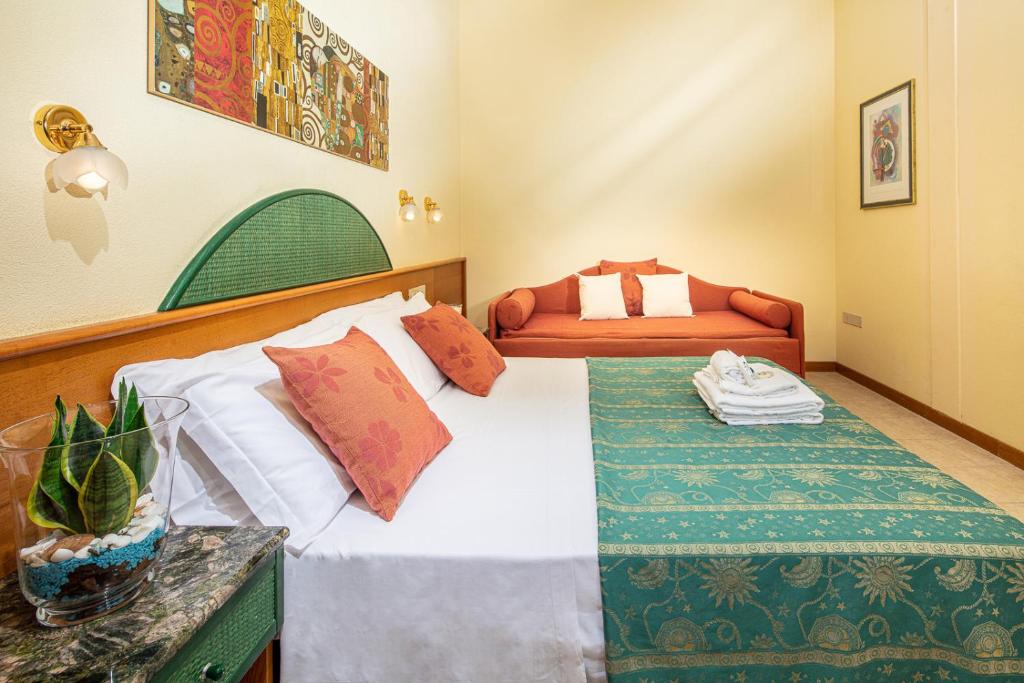 Mūsdienīgs viesnīcas numurs ar divguļamo gultu, sarkanu dīvānu un dekoratīvu mākslu uz sienas. Telpā ir zaļa gultas pārklājs un augi, kas rada patīkamu atmosfēru.