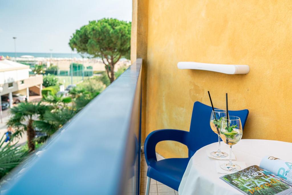 Balkons ar skatu uz pludmali, uz galda divas kokteiļu glāzes un žurnāls. Daba apvīta ar palmām un saulaina atmosfēra.