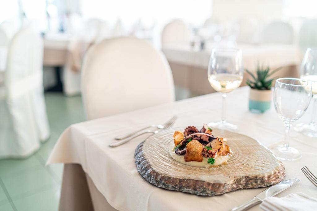 Elegants galda iestatījums ar sulīgu ēdienu, kas pasniegts uz koka griešanas dēļa, un vīna glāzēm. Svaigi sastāvdaļas un gaumīgs dizains piešķir restorāna atmosfērai.