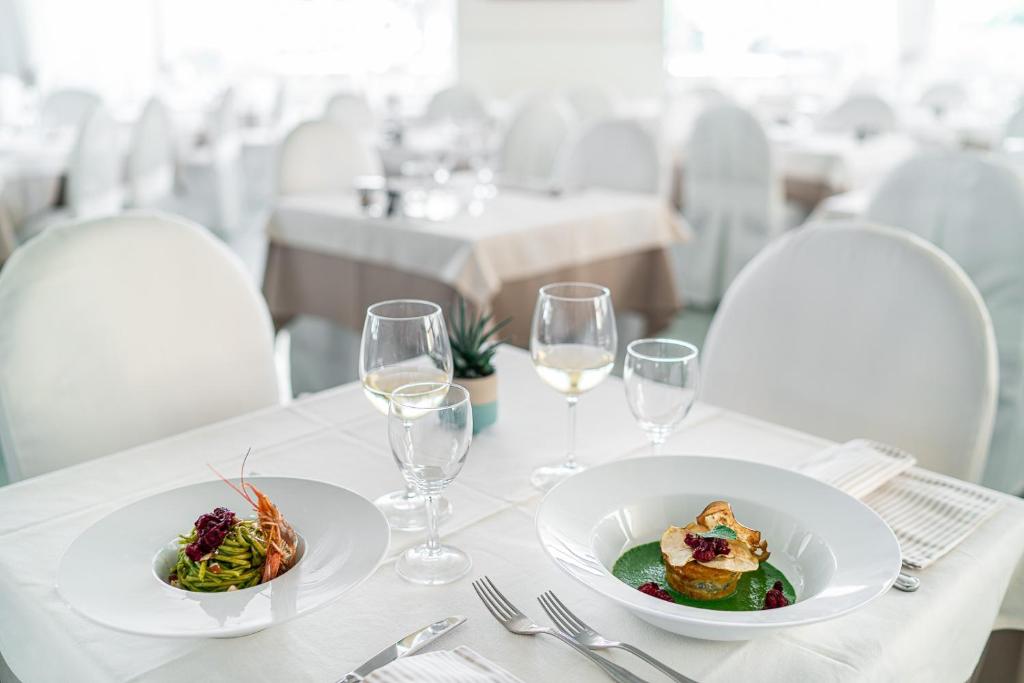 Elegants restorāna galds ar diviem izsmalcinātiem ēdieniem un vīna glāzēm. Galds ir klāts ar baltu galdautu, radot mierīgu un stilīgu atmosfēru.