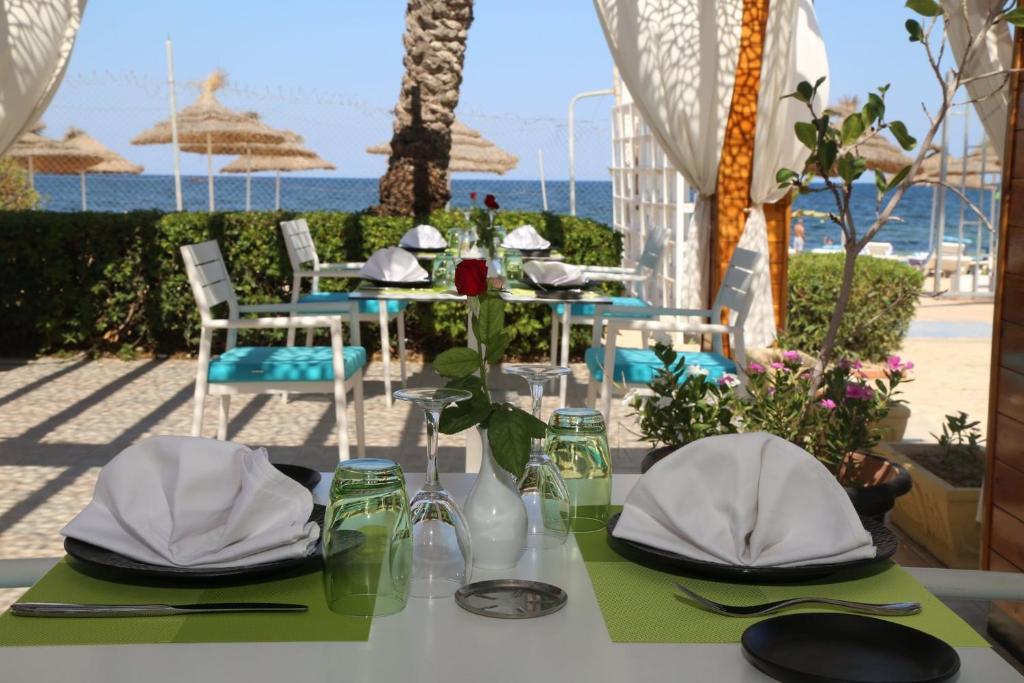 Pludmales restorāns ar galdiem, kas rotāti ar ziediem un elegantām galda piederumiem. Skats uz jūru un saulainu laiku rada patīkamu atmosfēru.
