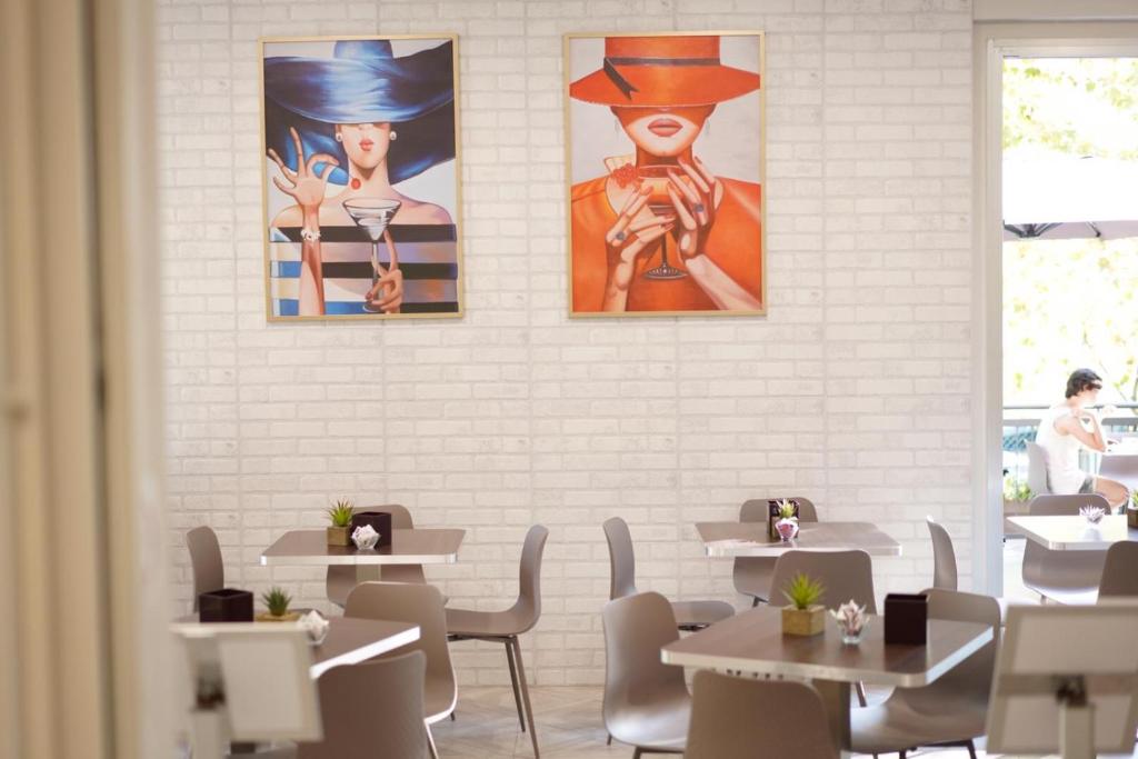 Mūsdienīgs restorāns ar elegantu interjeru, kurā redzamas divas krāsainas gleznas ar sievietēm, kas tur dzērienus. Galdiņi ir vienkārši un stilīgi, radot patīkamu atmosfēru.