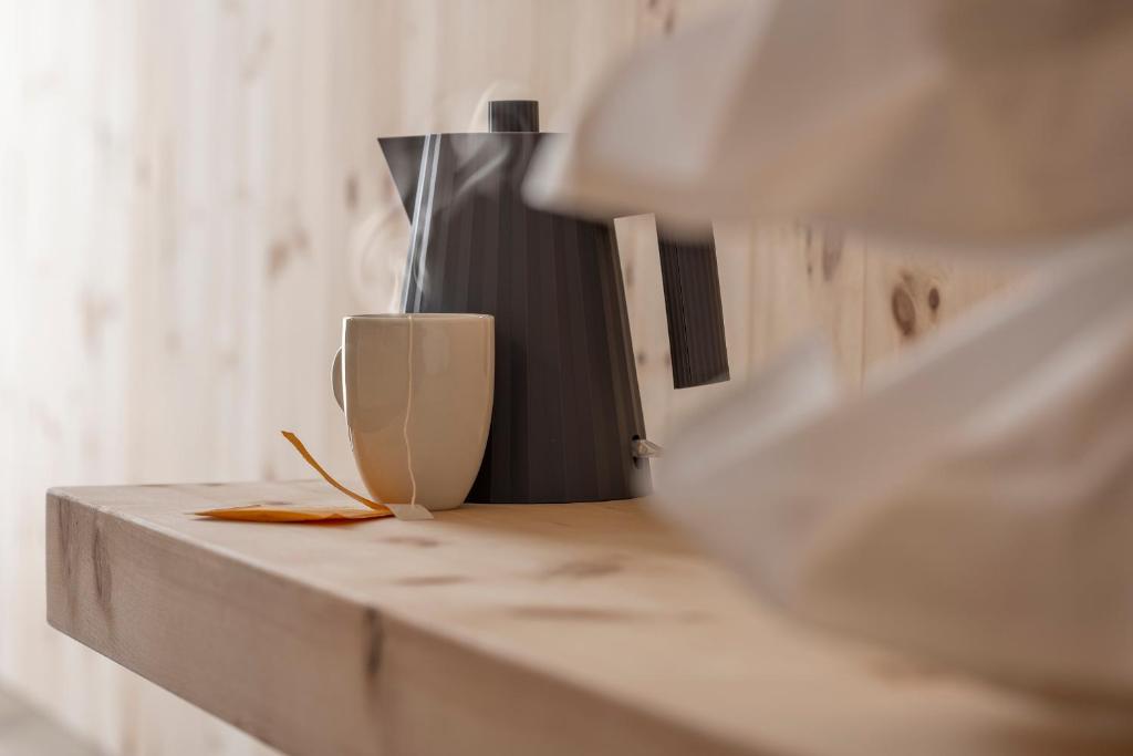 Tējkanna un tase ar tvaiku uz koka galda, papildināta ar žāvētu lapu.