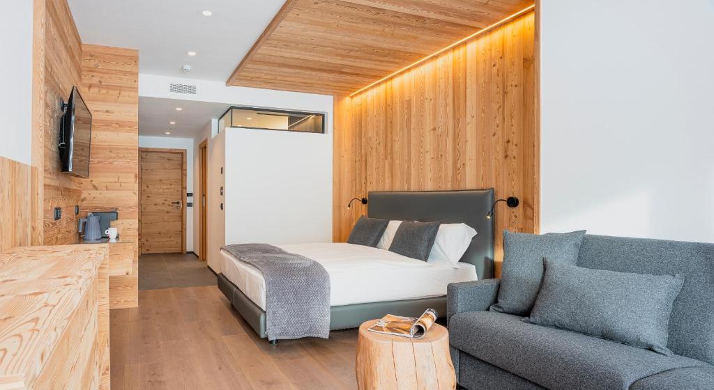 Mūsdienīgs guļamistabas interjers ar koka apdari, gultu un ērtu dīvānu. Telpa ir gaiša un silta ar siltu apgaismojumu.