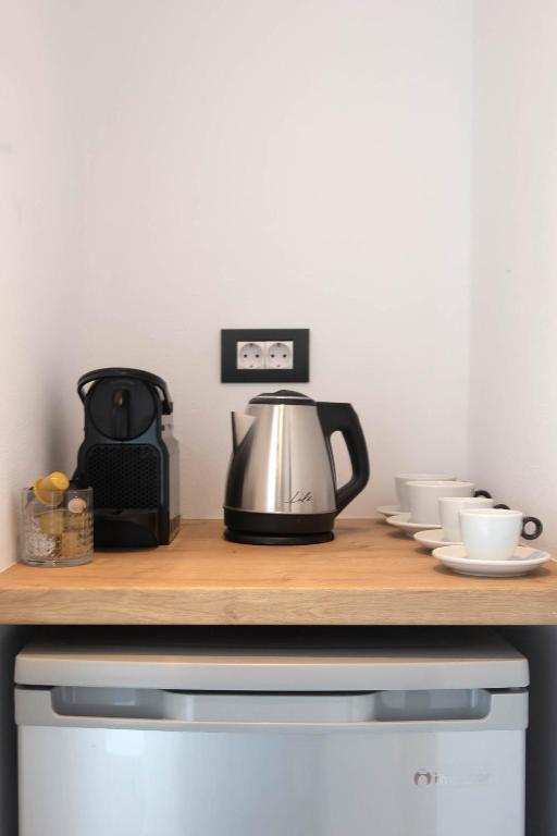 Kafijas stūra ar tējkannu, kafijas aparātu un kausu komplektu, uz koka virsmas, blakus ledusskapim. Ideāla vieta dzērienu pagatavošanai.