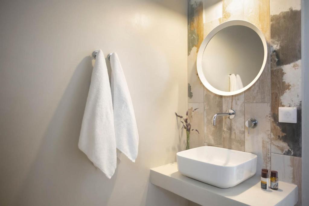 Mūsdienīgs vannas istabas interjers ar apaļu spoguli, elegantu izlietni un baltām dvieli. Dabas elementu akcenti piešķir telpai siltumu un komfortu.