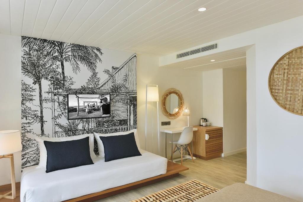 Mūsdienīgs viesnīcas numurs ar stilīgu melnbaltu sienu gleznojumu, kurā attēlotas palmas un ainava, kā arī televizors un ērts dīvāns. Interjers ir gaišs un elegants, ar koka akcentiem un minimālistisku dizainu.