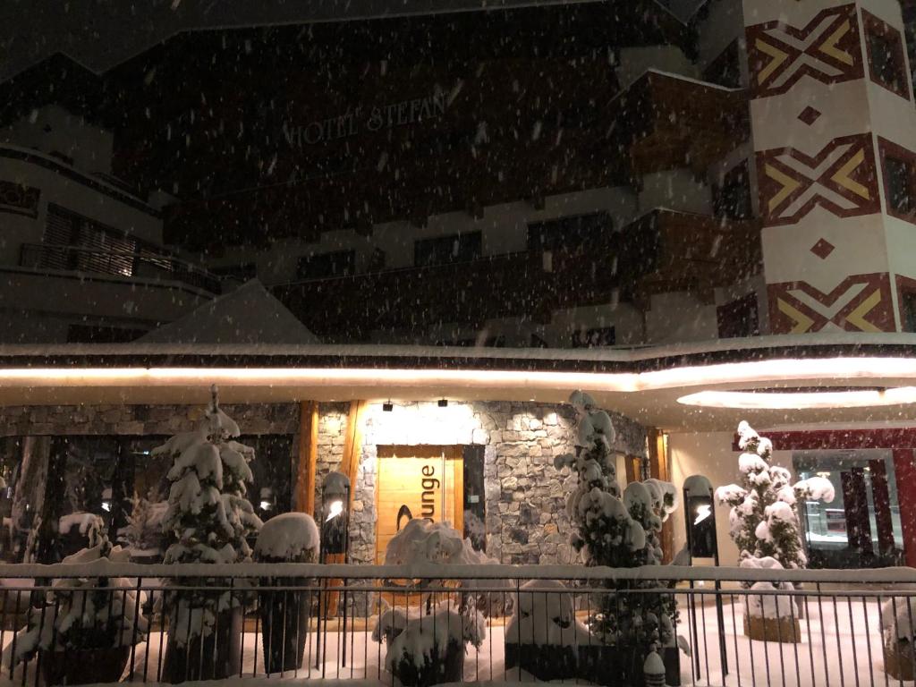 Ziemas ainava pie viesnīcas "Stefan", kur sniegs klāj visu apkārtni un rotā koku zarus, radot burvīgu atmosfēru. Apgaismojums pie ieejas piešķir siltumu un aicina apmeklētājus.