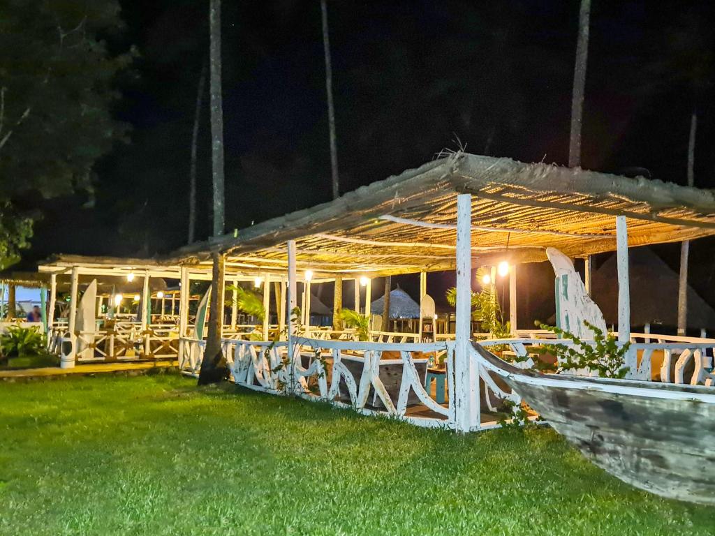 Nakts ainava ar koka terasi, kas apgaismota ar lampām un ieskauta zaļā zālē. Šī vieta izskatās kā ideāla vieta relaksācijai un vakariņām dabā.